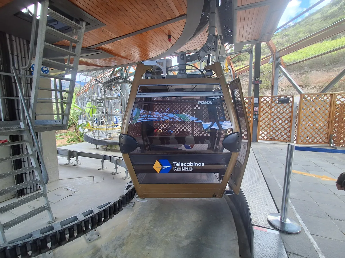 A gondola cabin of the Telecabinas Kuélap cable car, branded with the cable-car operator's logo, docked at the upper station with hillside visible through the open doors